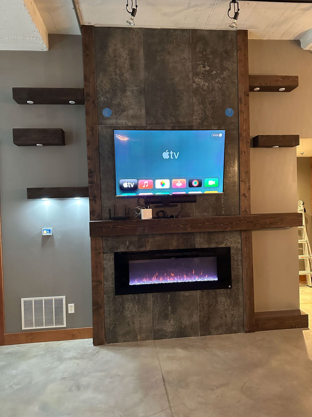 Modern living room wall with mounted flat-screen TV showing Apple TV interface and a rectangular electric fireplace below.