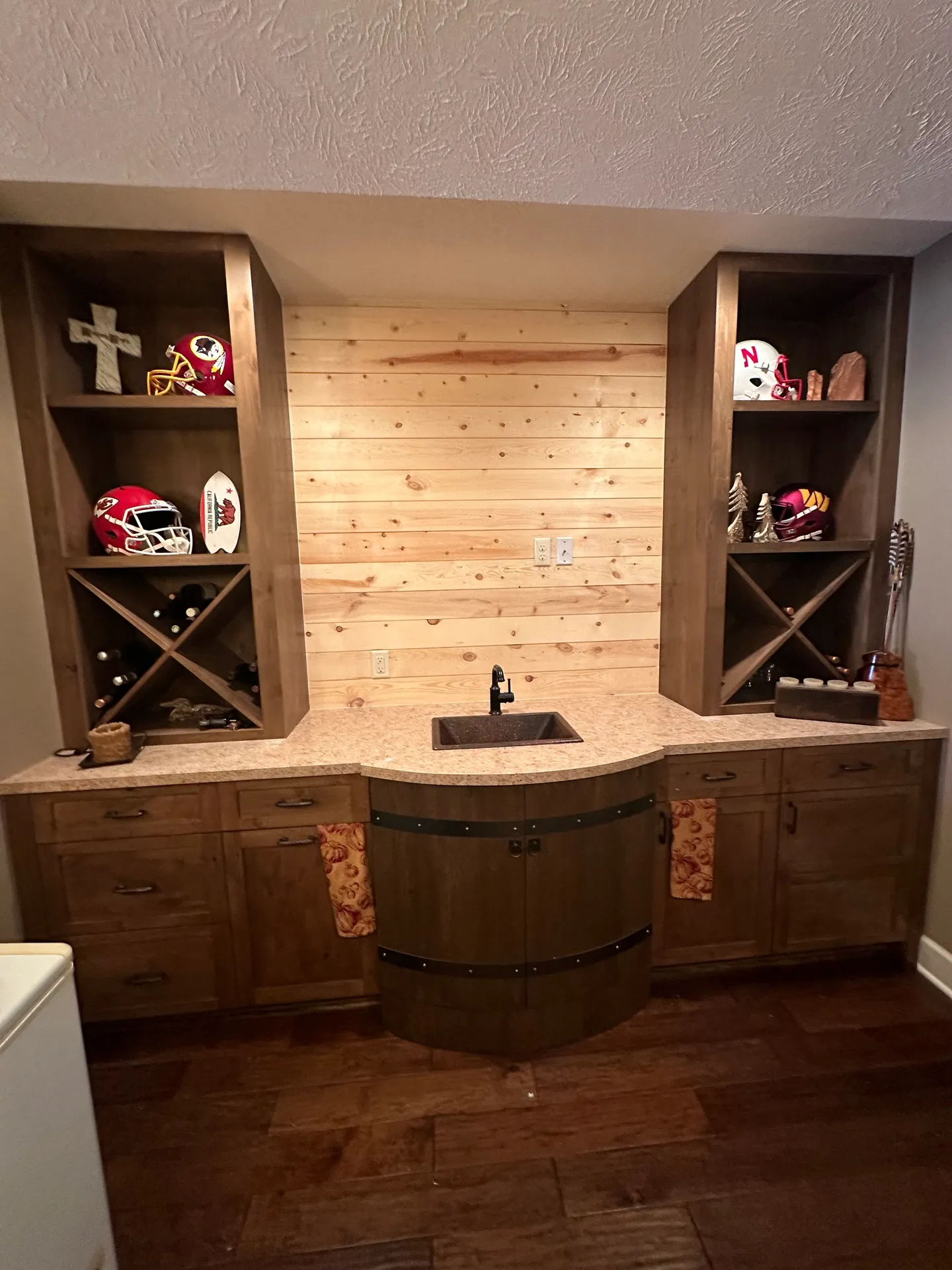 Wooden bar area with wine racks, sports helmets, a small sink, and wooden wall paneling in the background.