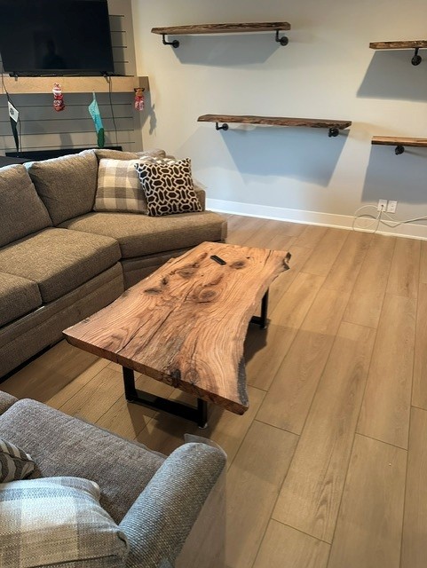 Living room with gray sectional sofa, patterned cushions, a natural wood coffee table with black metal legs, floating wooden shelves on the wall, and a TV mounted above a fireplace mantel with hanging Christmas stockings.