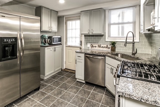 Modern kitchen with stainless steel refrigerator, dishwasher, gas stove, granite countertops, and white cabinets.